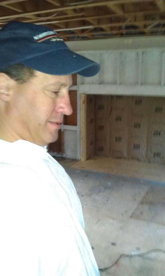 A man in white shirt and hat standing next to wall.