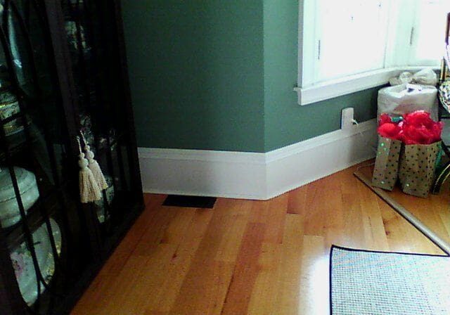 A corner of the room with green walls and wood floors.